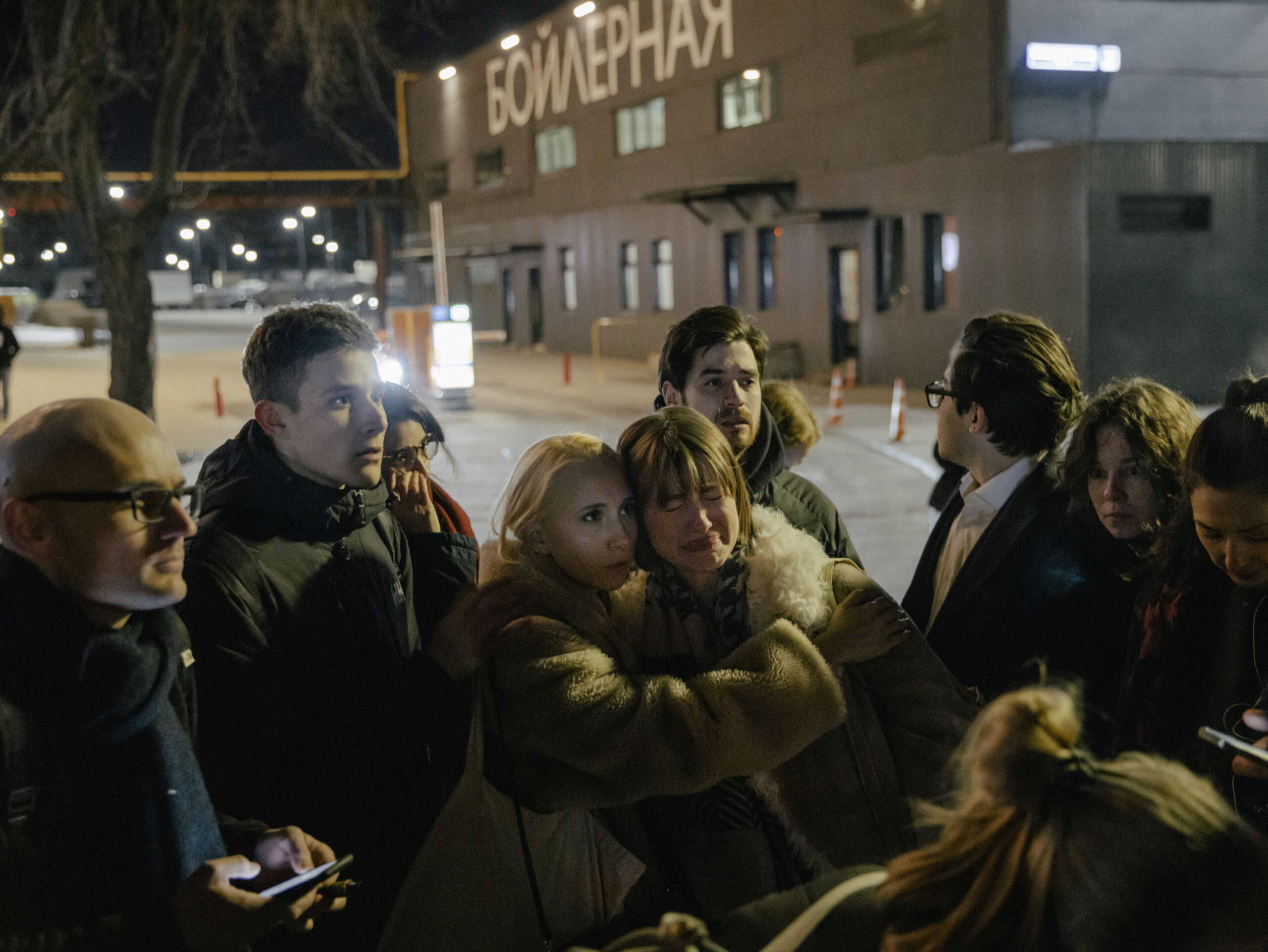 a group of journalists are huddling outside their studio on a cold, dark night, looking scared 